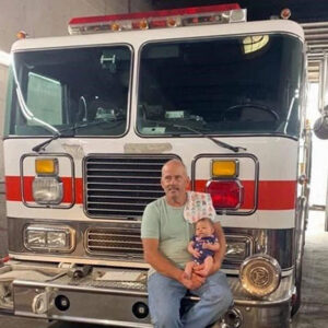 a man holding a baby with a truck behind them